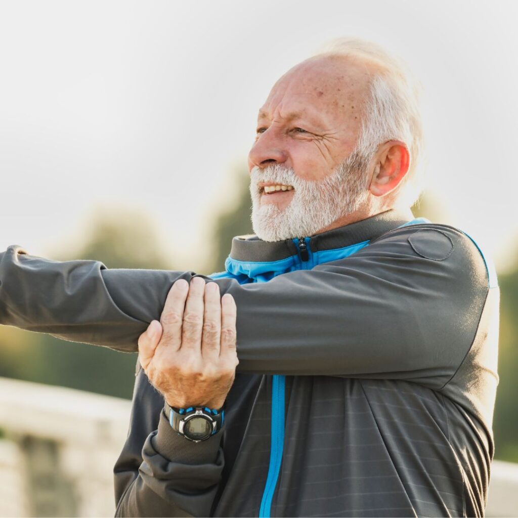 older man in athletic wear stretching shoulder and smiling